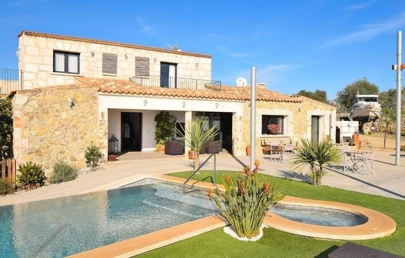 Villa de piedra con piscina y patio ajardinado bajo un cielo azul brillante.