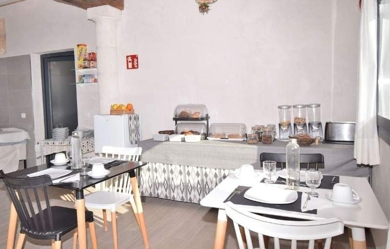 Comedor con mesa de buffet, sillas blancas y una pequeña encimera de cocina en una habitación luminosa.