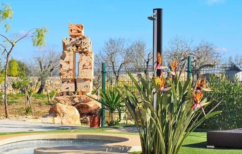 Paisaje con una fuente de piedra, un poste negro alto y flores naranjas en un jardín soleado.