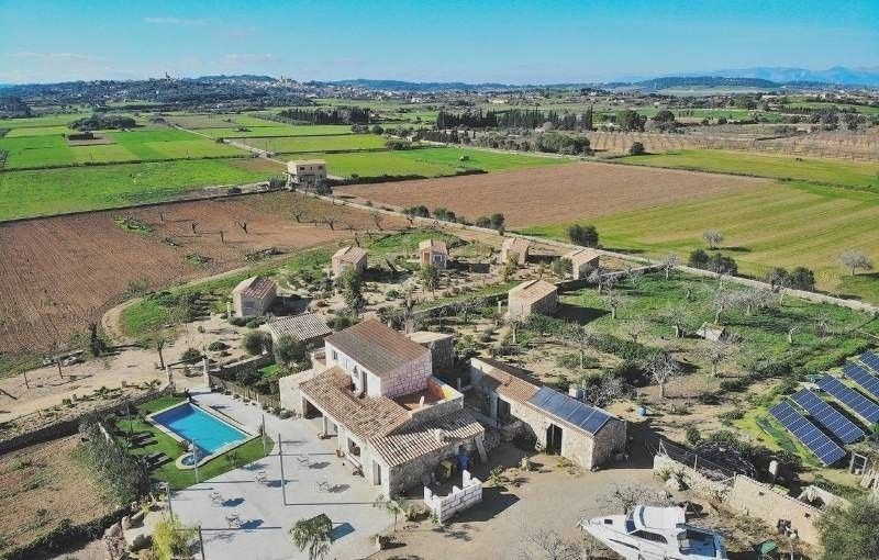 Vista aérea de una casa de campo rural y sus dependencias junto a campos verdes y tierras de cultivo.