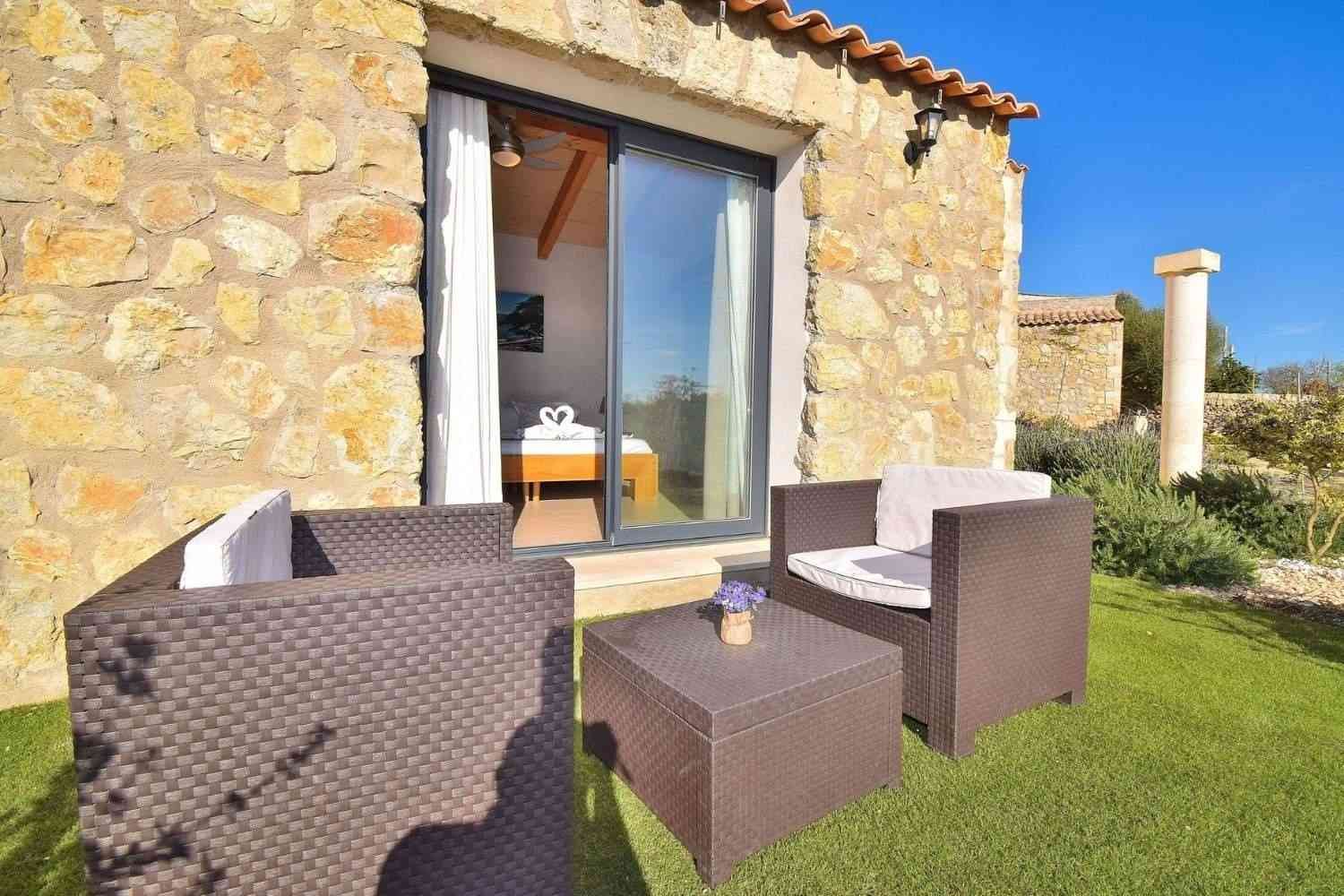 Patio de piedra con sillas de mimbre, césped verde y vistas soleadas al jardín.