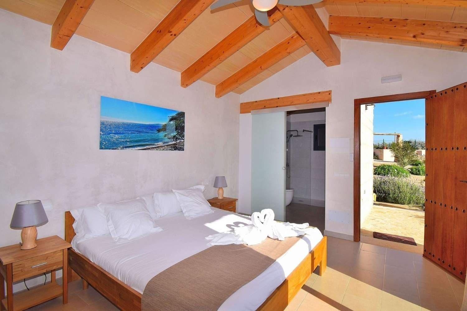 Habitación luminosa con vigas de madera, cama doble, cuadro con motivos marinos y ventana con cortinas.
