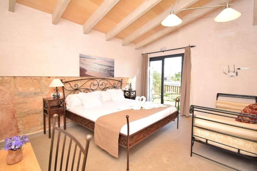 Habitación luminosa con cama de madera, ventana grande y literas bajo techo abovedado.