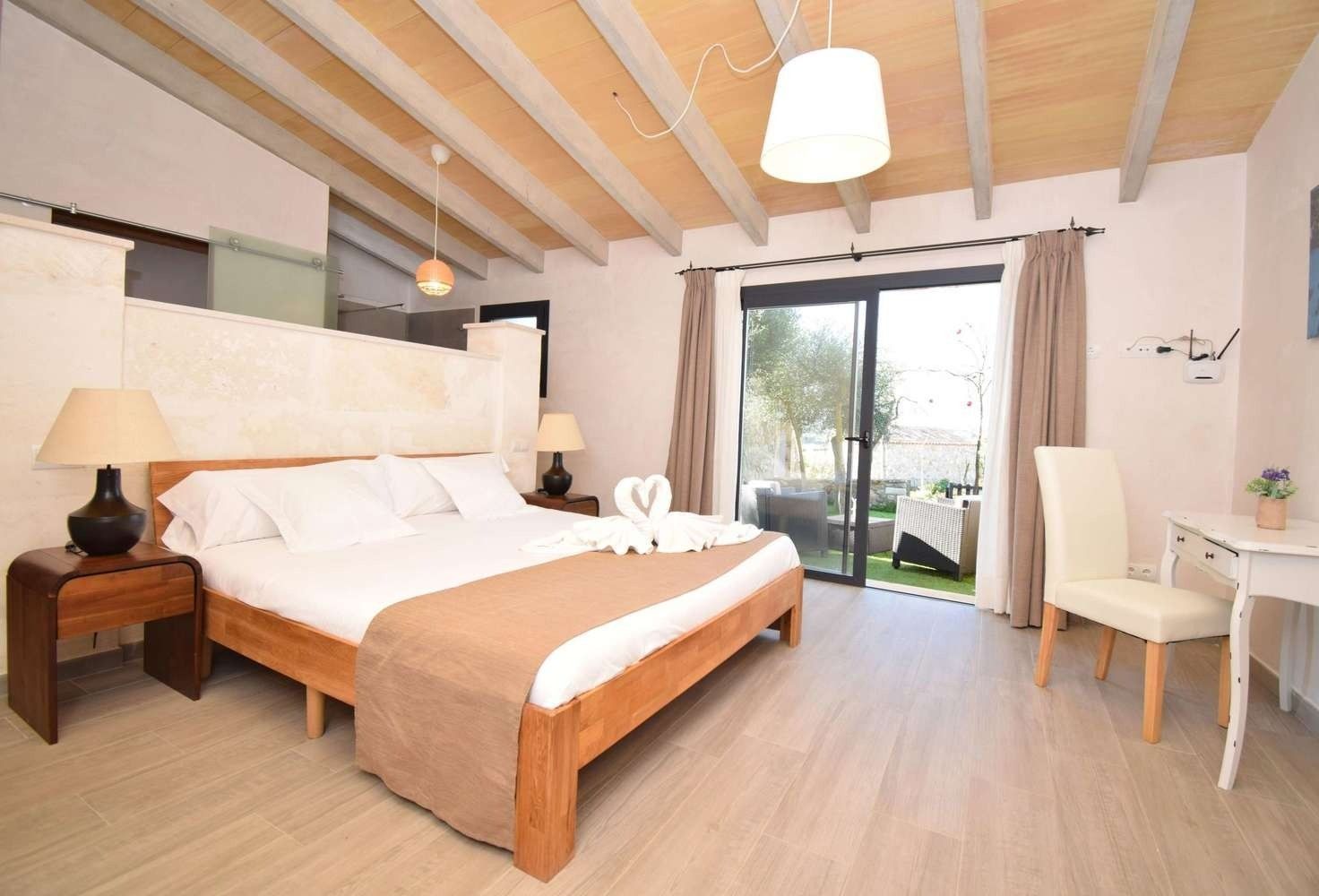 Habitación luminosa con cama de madera, escritorio, silla y puertas correderas de cristal que dan a un balcón.