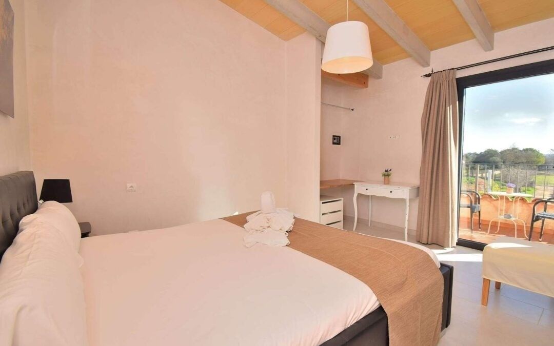Habitación luminosa con cama, escritorio, puerta de balcón y vistas a la montaña.