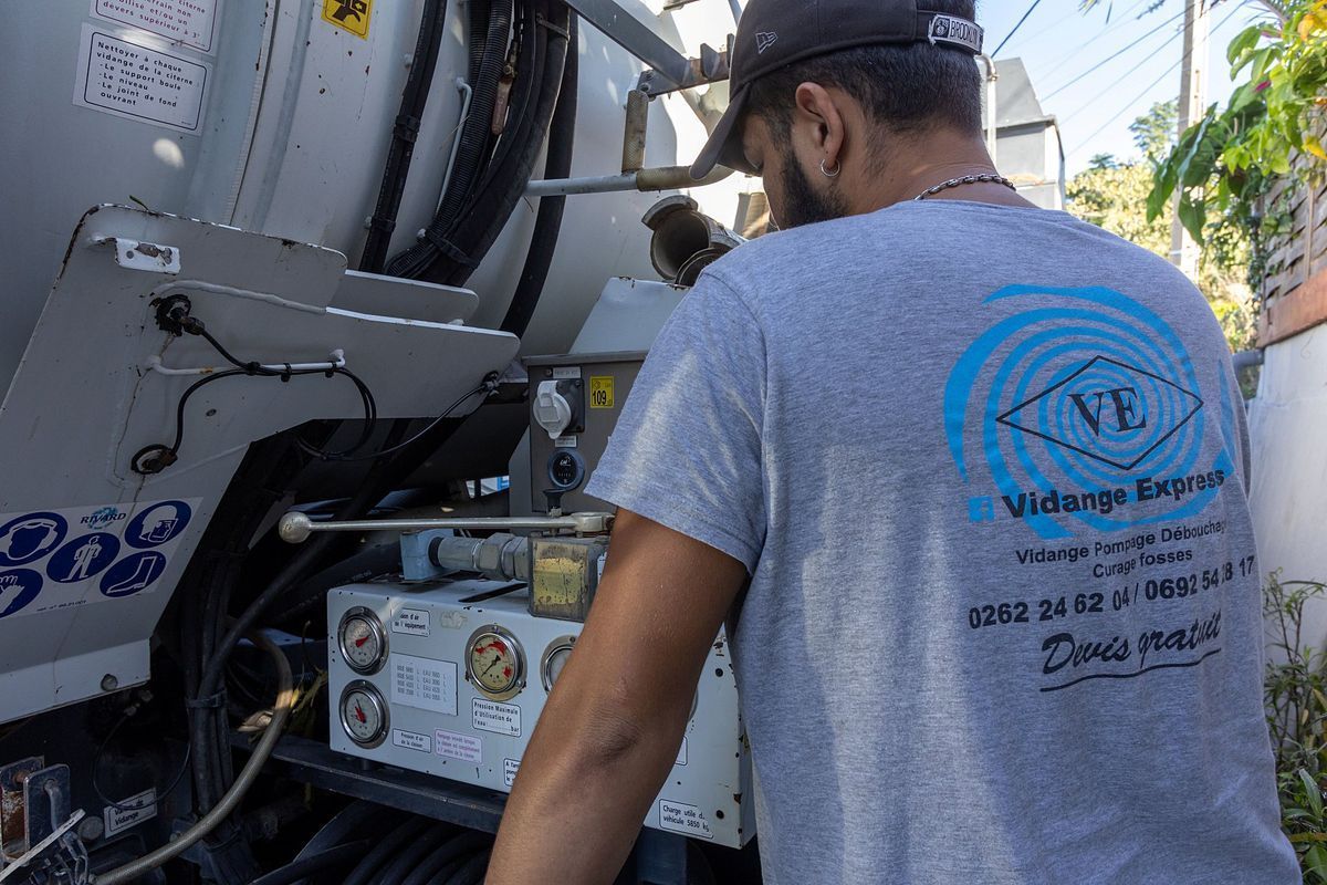 Professionnel portant un haut de Vidange Express à l'arrière d'un camion de vidange.