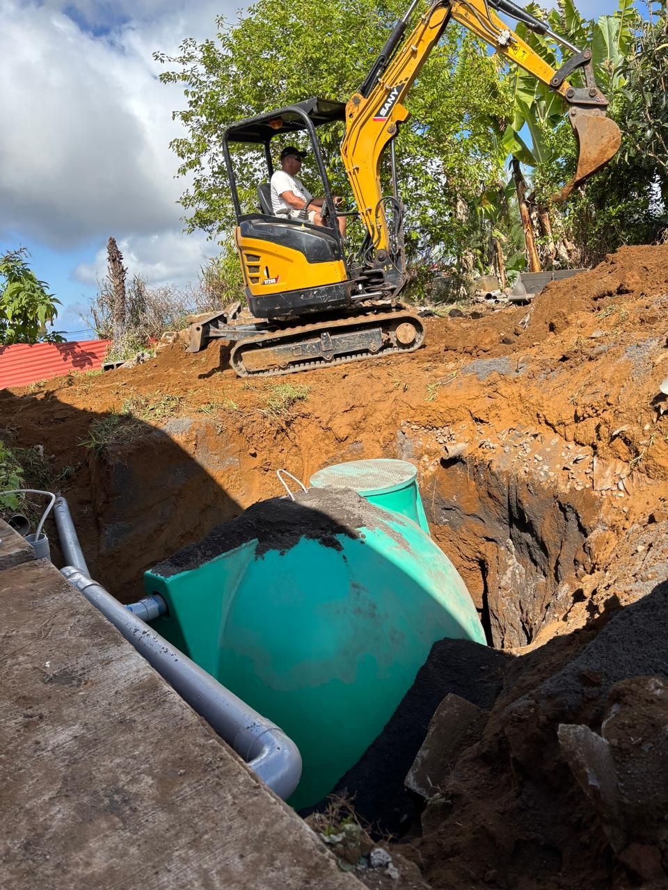 Cuve enterrée verte avec un engin de chantier orange à proximité.