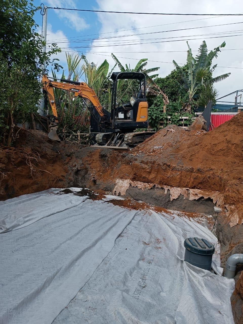 Tractopelle orange sur un chantier de mise aux normes d'une fosse septique.