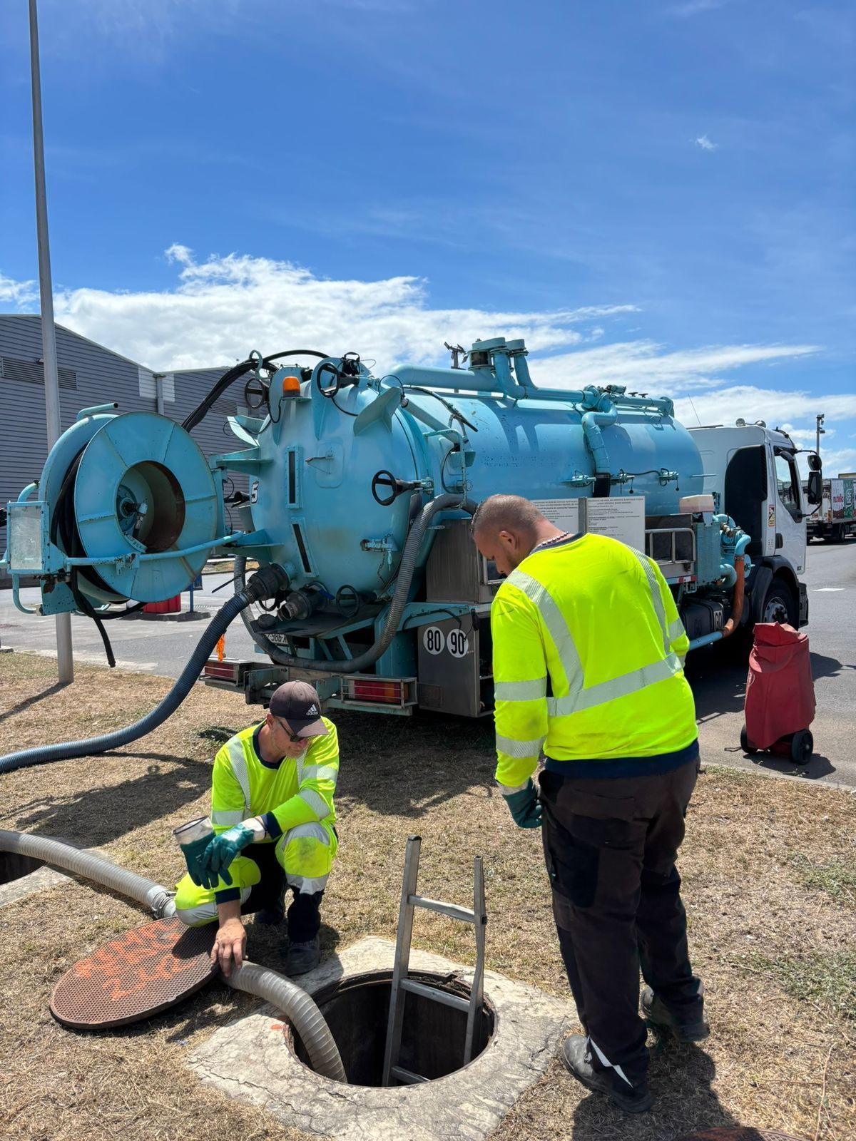 Professionnels derrière un camion de vidange et observant l'entrée d'une canalisation.