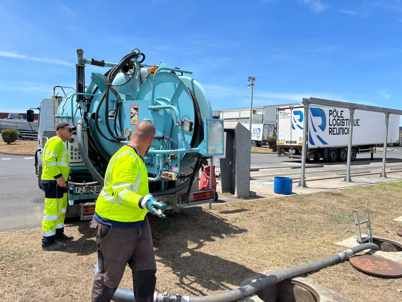 Deux professionnels en jaune à l'arrière d'un camion bleu clair qui manipulent des tuyaux de vidange.