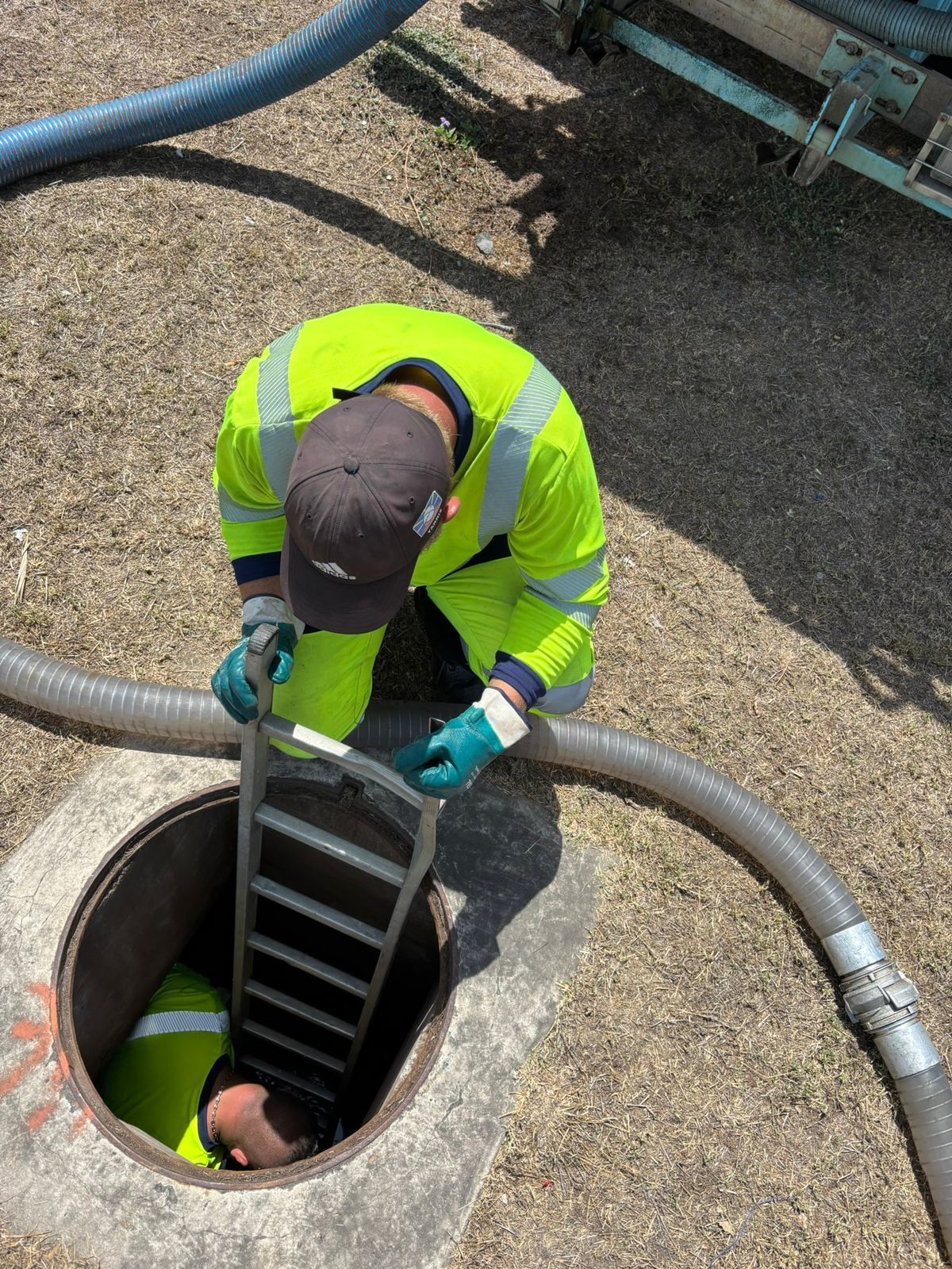 Professionnel tenant une échelle pour un collègue dans une bouche d'égout.