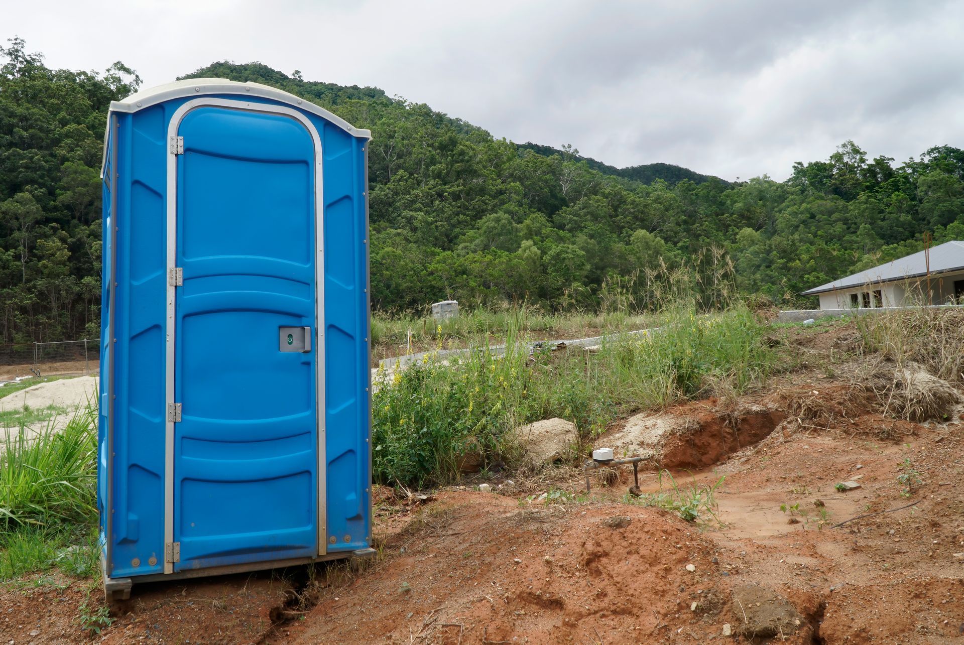 WC de chantier bleu posé sur un terrain près d'une forêt.