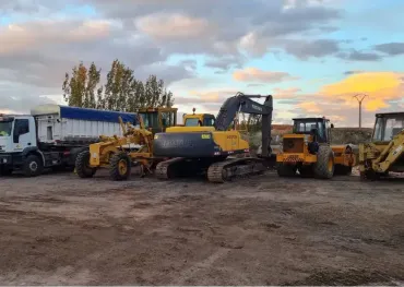 Un grupo de vehículos de construcción están estacionados en un campo de tierra.