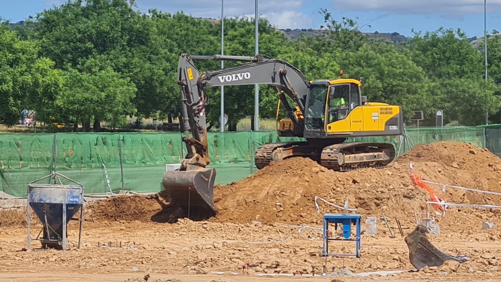 Una excavadora amarilla está cavando un hoyo en un campo de tierra.