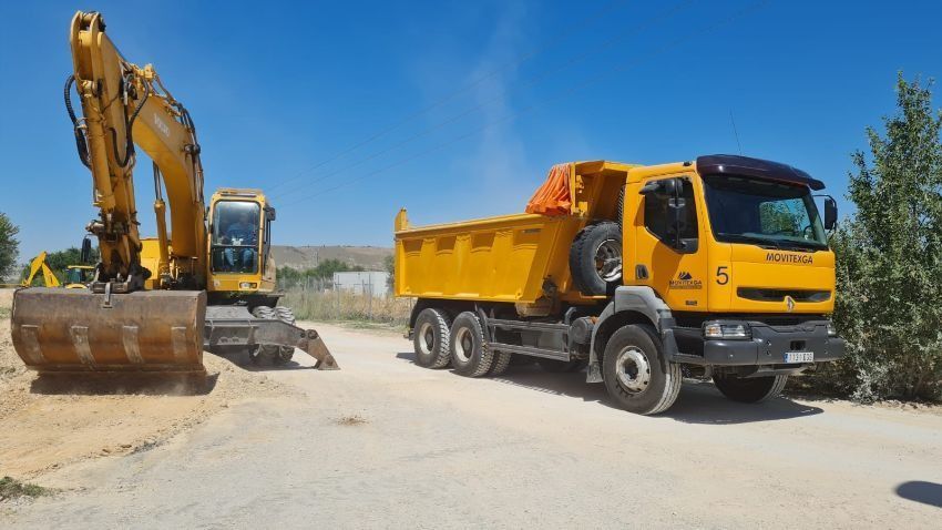 Un camión volquete amarillo está estacionado junto a una excavadora amarilla en un camino de tierra.