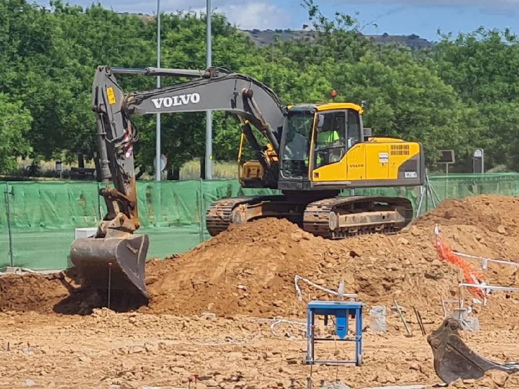 Una excavadora Volvo amarilla está cavando un hoyo en un campo de tierra.
