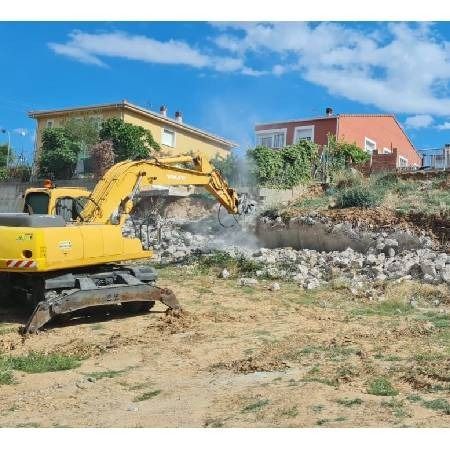 Una excavadora amarilla está demoliendo un edificio en un campo.