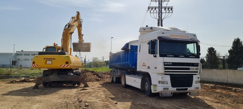 Un camión blanco está estacionado junto a una excavadora amarilla en un camino de tierra.