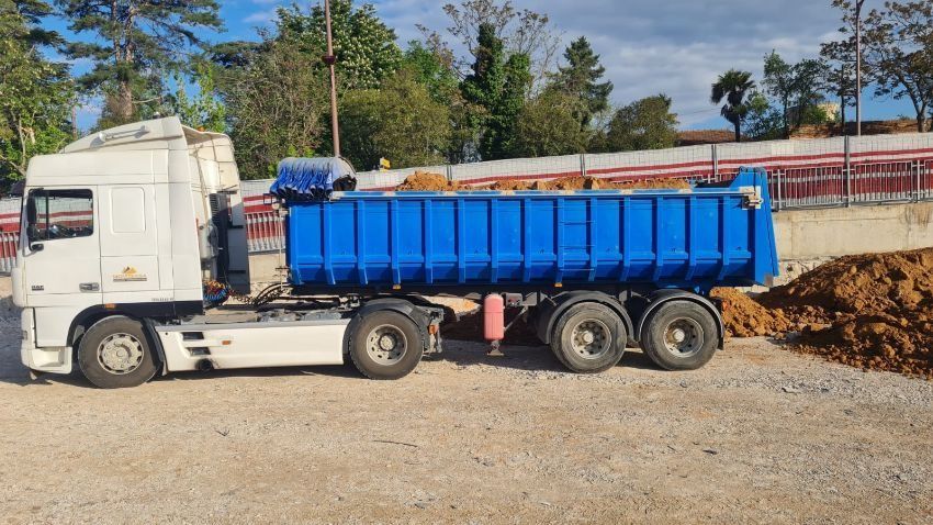 Un camión de volteo está estacionado en un lote de grava al lado de un montón de tierra.