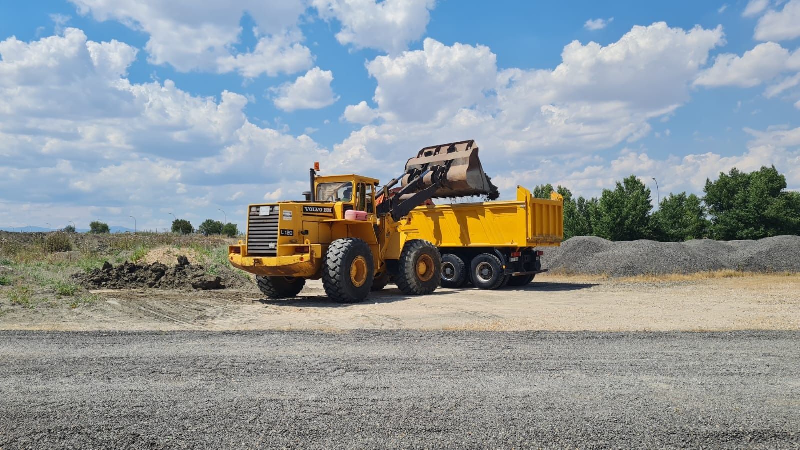 Un camión volquete amarillo circula por un camino de grava.