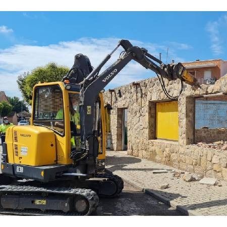 Una excavadora amarilla está demoliendo un edificio de piedra.