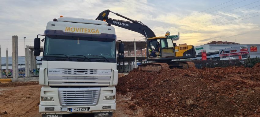 Un camión blanco está estacionado en un campo de tierra al lado de una excavadora grande.