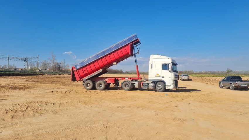 Un camión de volteo está estacionado en un campo de tierra al lado de un automóvil.