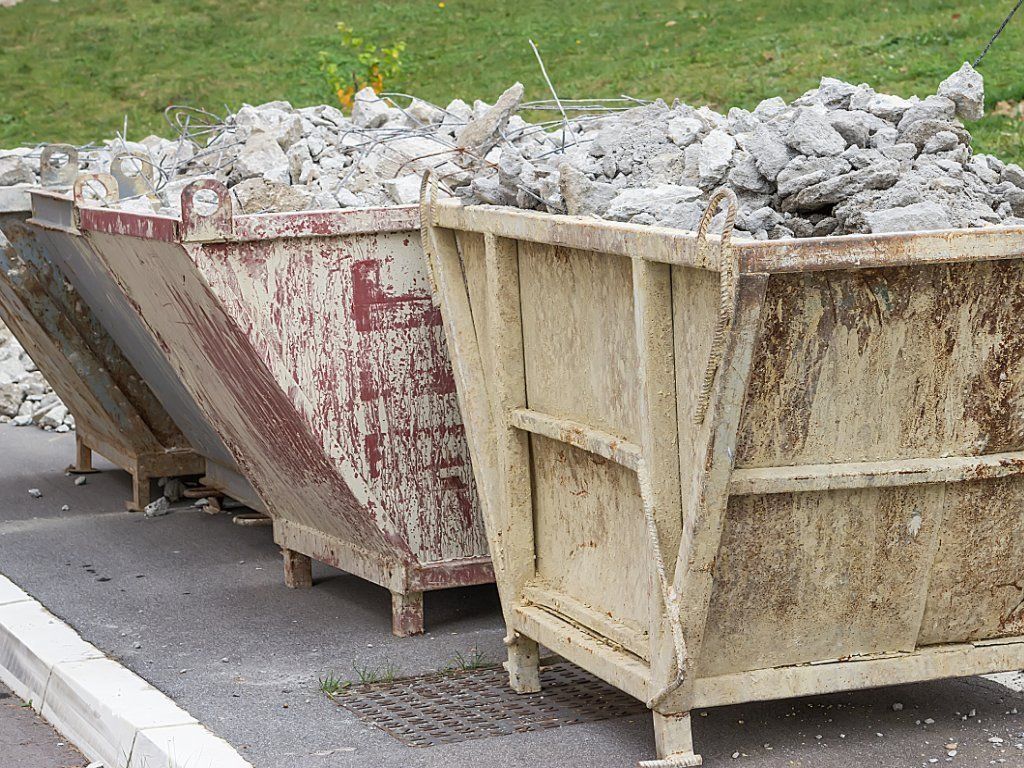 Hay dos contenedores llenos de piedras tirados al costado de la carretera.