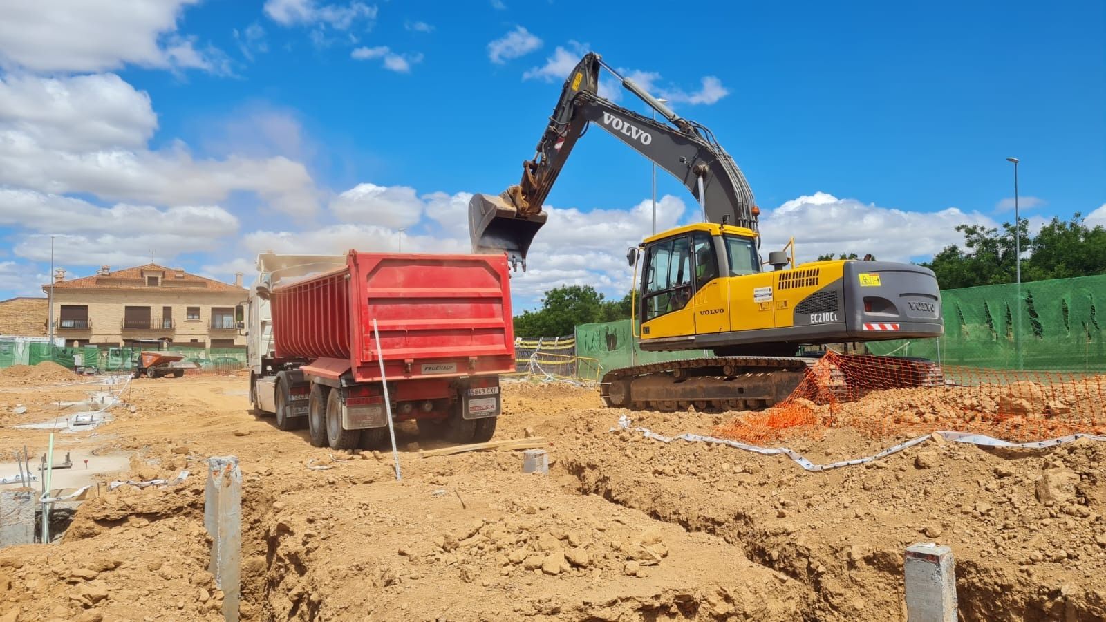 Una excavadora amarilla está cargando tierra en un camión volquete rojo.