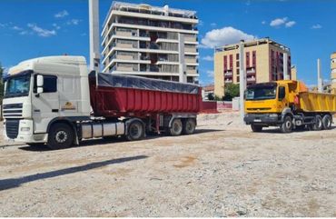Dos camiones de volteo están estacionados en un lote de grava