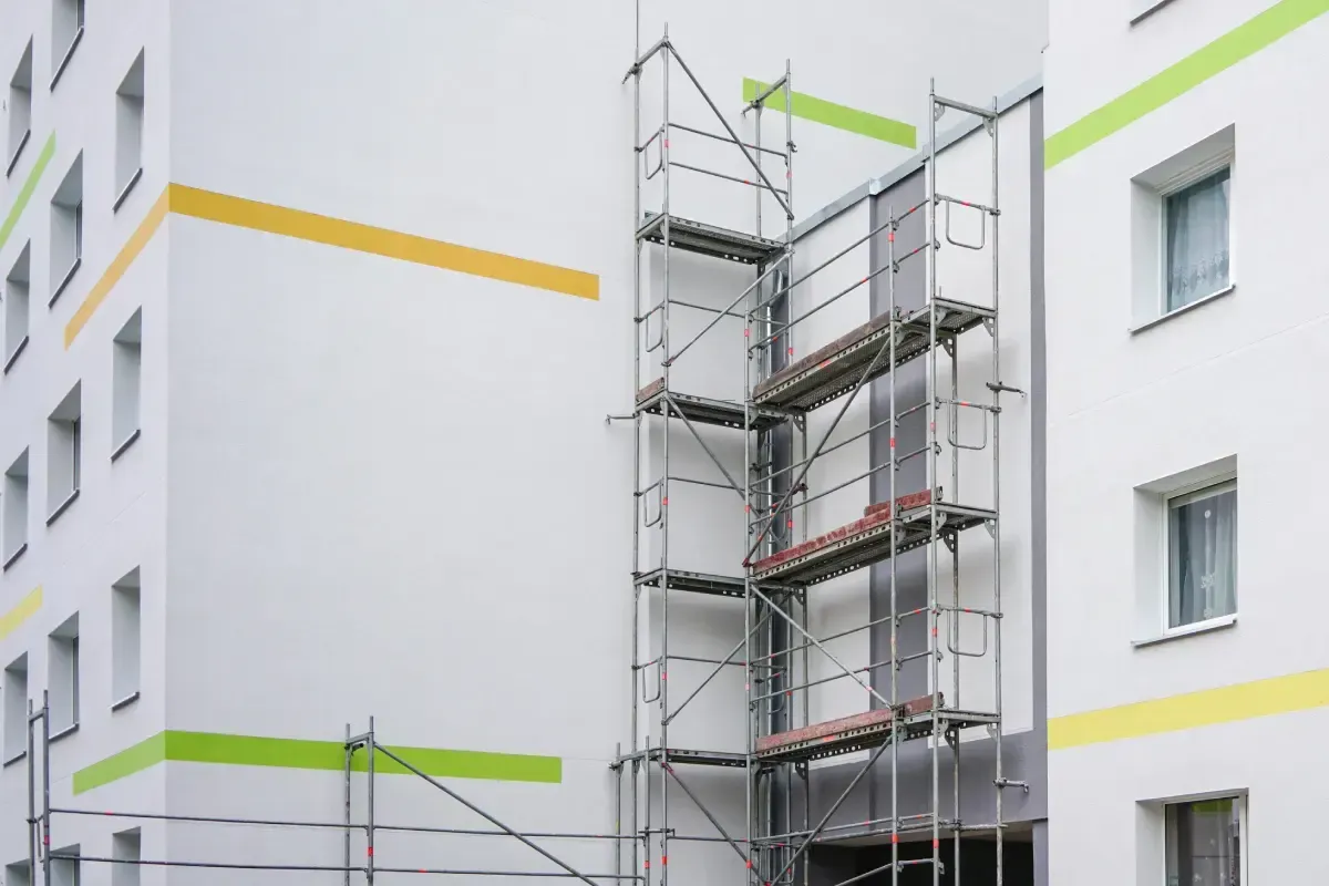 Un andamio metálico se alza contra la pared exterior de un edificio blanco