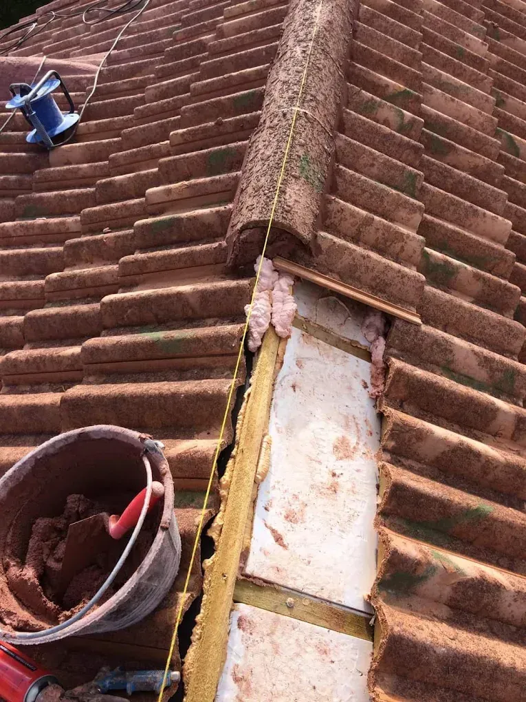 Reparación en curso en un tejado de tejas rojas, donde se observa una sección de tejas de cumbrera retirada