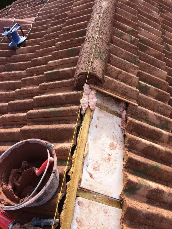 Reparación en curso en un tejado de tejas rojas, donde se observa una sección de tejas de cumbrera retirada