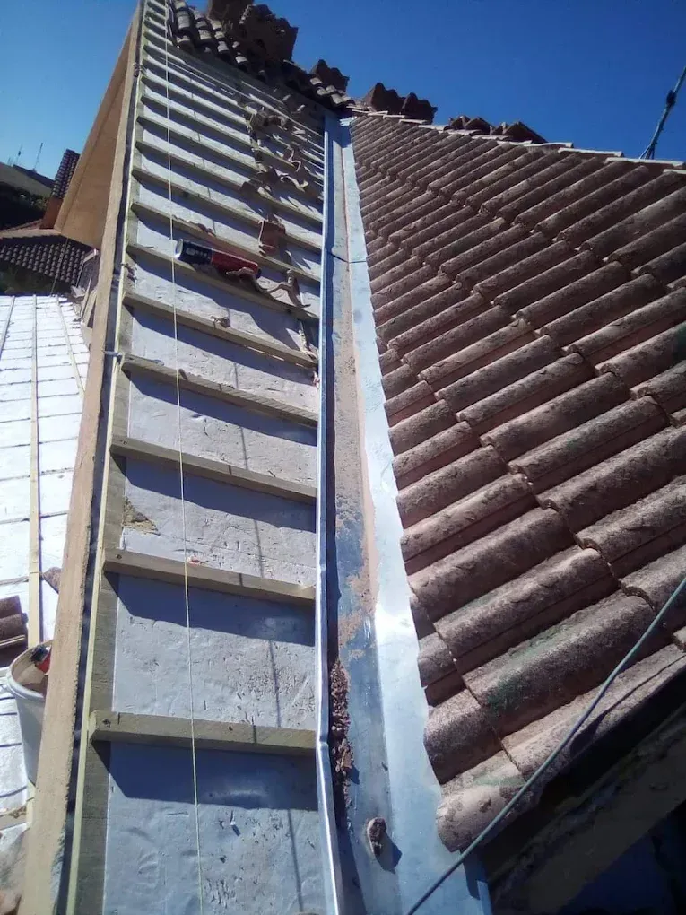 Un tejado a media teja en construcción que muestra una canaleta metálica entre un marco de madera