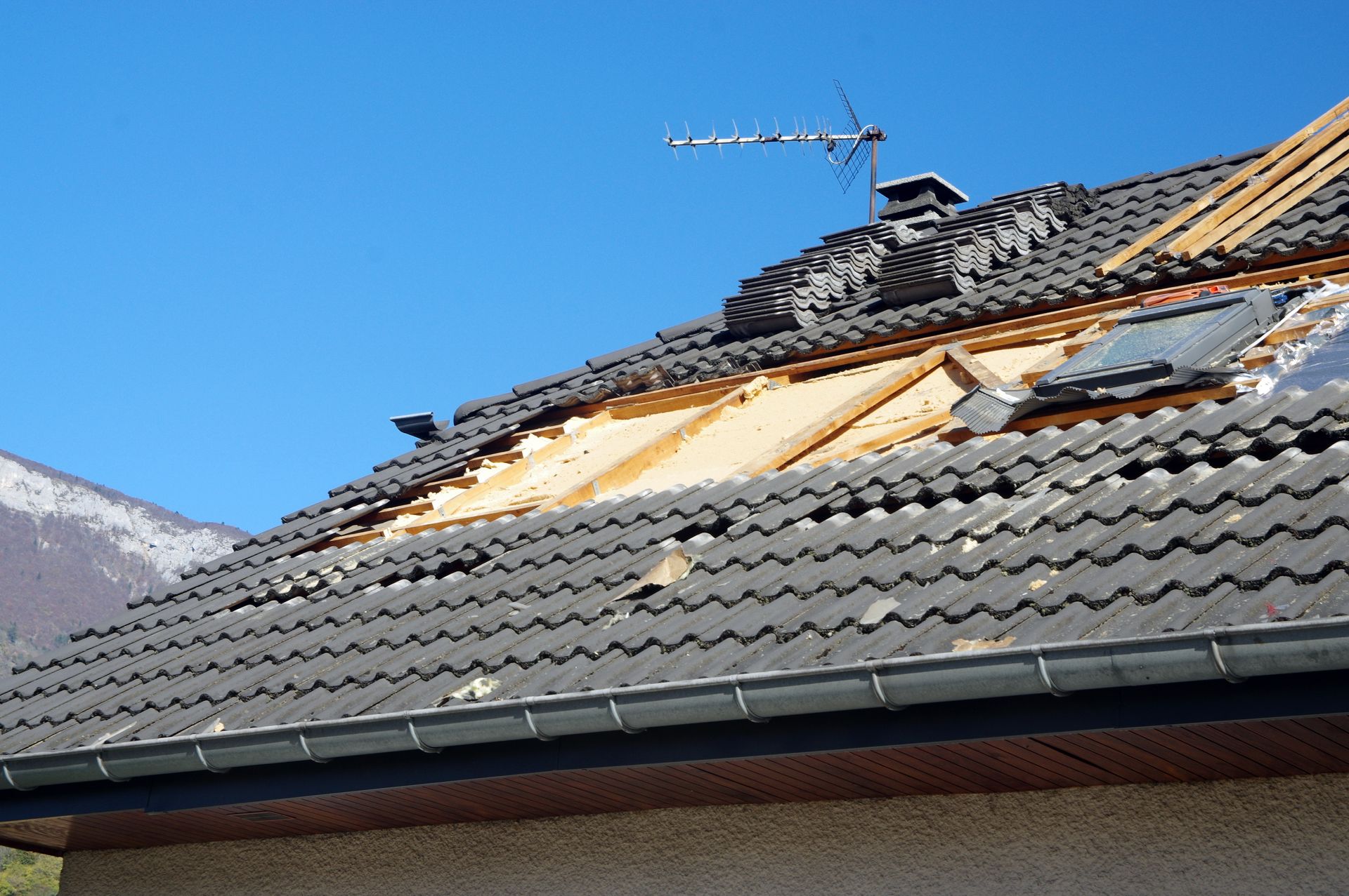 Toiture d'une maison partiellement endommagée, avec des tuiles manquantes, révélant une charpente en bois.