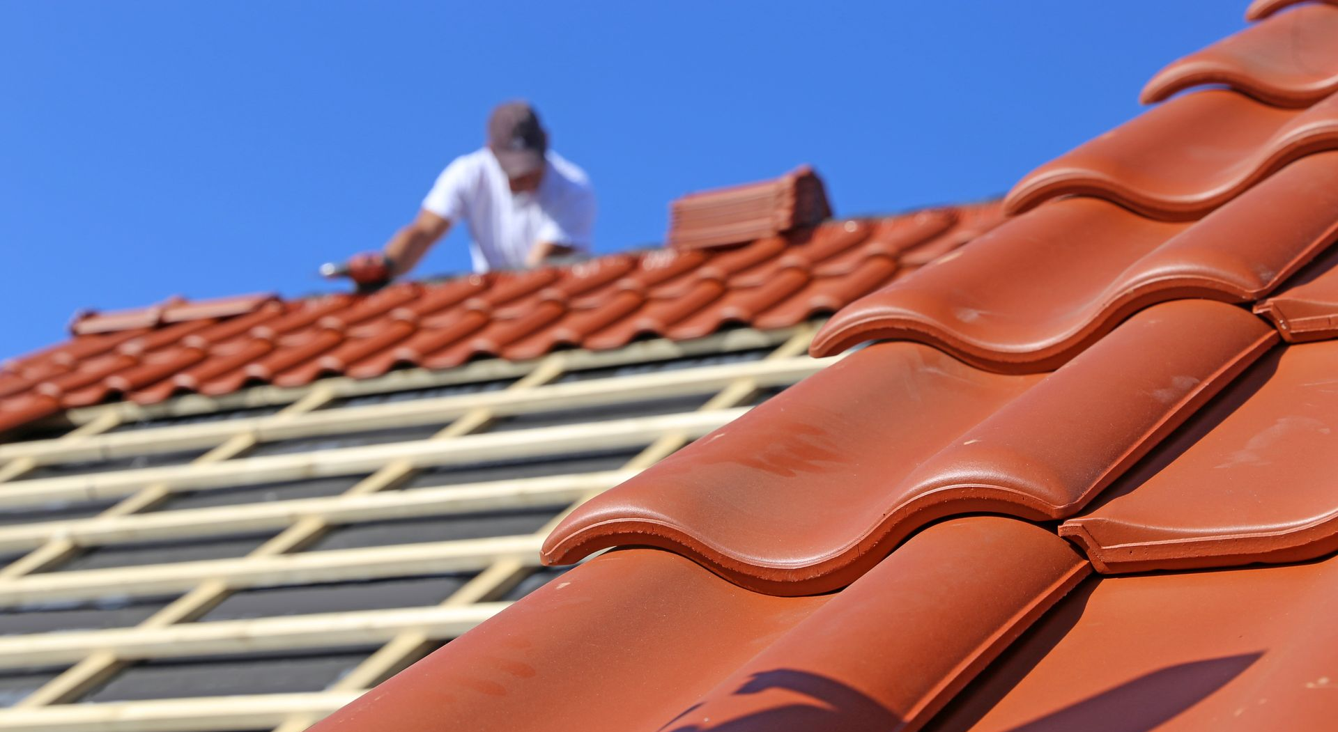Un couvreur pose un toit de tuiles rouges par une journée ensoleillée.