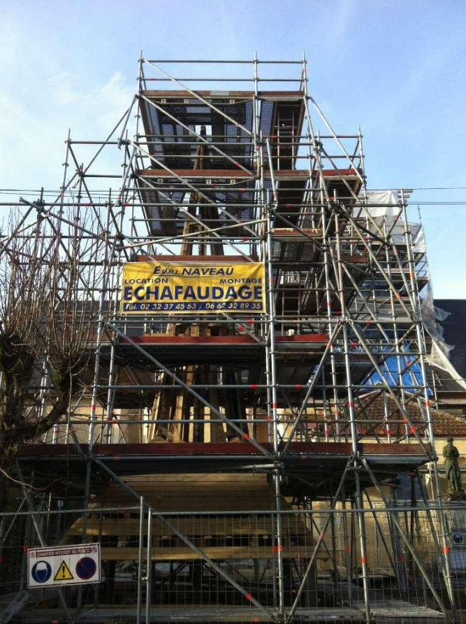 Des échafaudages entourent un bâtiment en rénovation, avec une banderole jaune de l'entreprise.