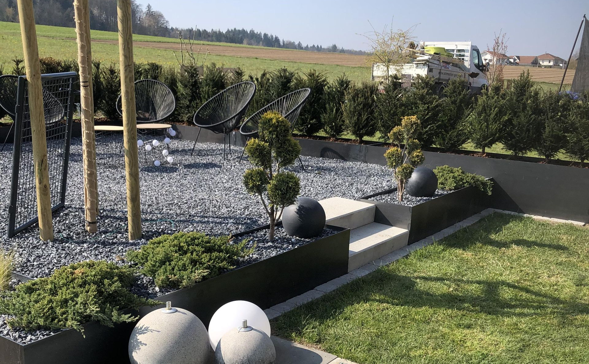 Terrasse mit Tisch und Stühlen, Markise und Pflanzen vor einem Gebäude.