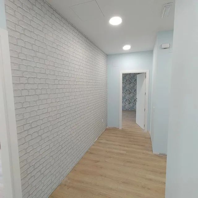 Un pasillo con una pared de ladrillo y piso de madera que conduce a una puerta.