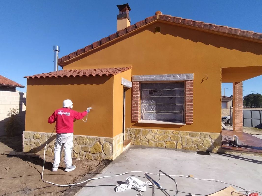 Un hombre con una camisa roja está pintando el costado de una casa.