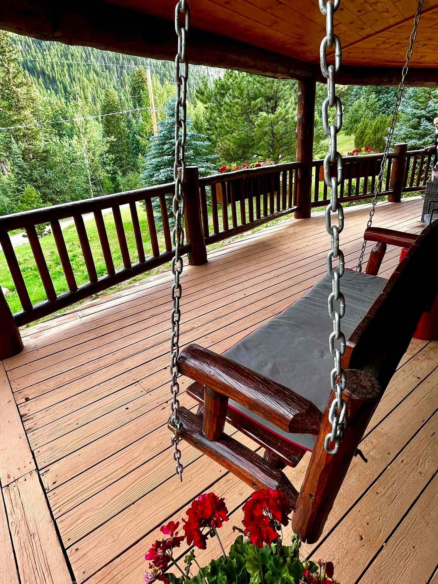 Porch swing and geraniums on the wrap-around deck at The Riverside Cabin in Allenspark, Colorado