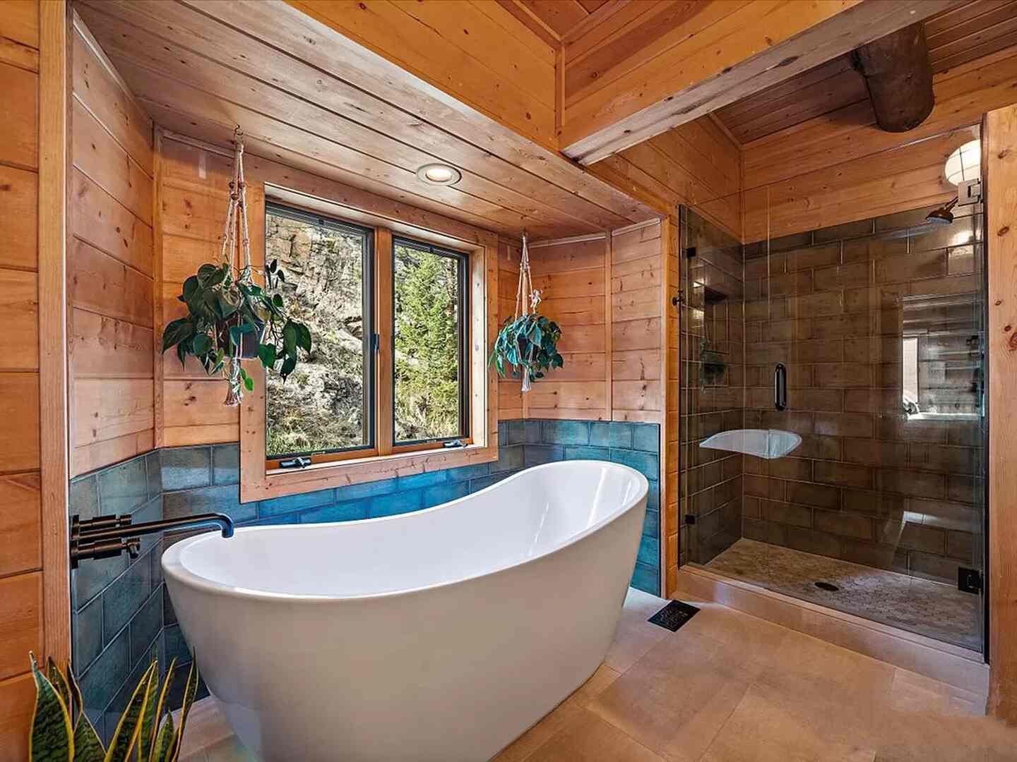 Freestanding soaking tub and blue tile bath with forest views at The Riverside Cabin