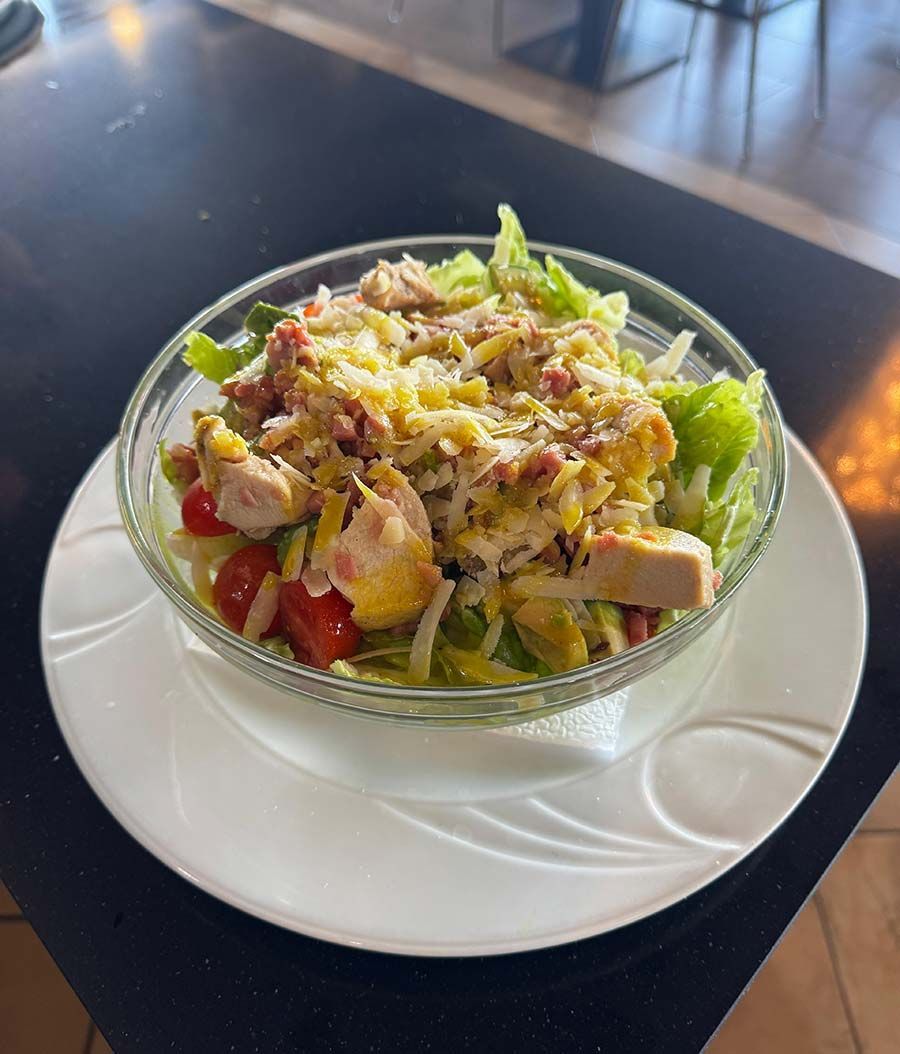 Una ensalada en un recipiente de vidrio sobre un plato blanco sobre una mesa.