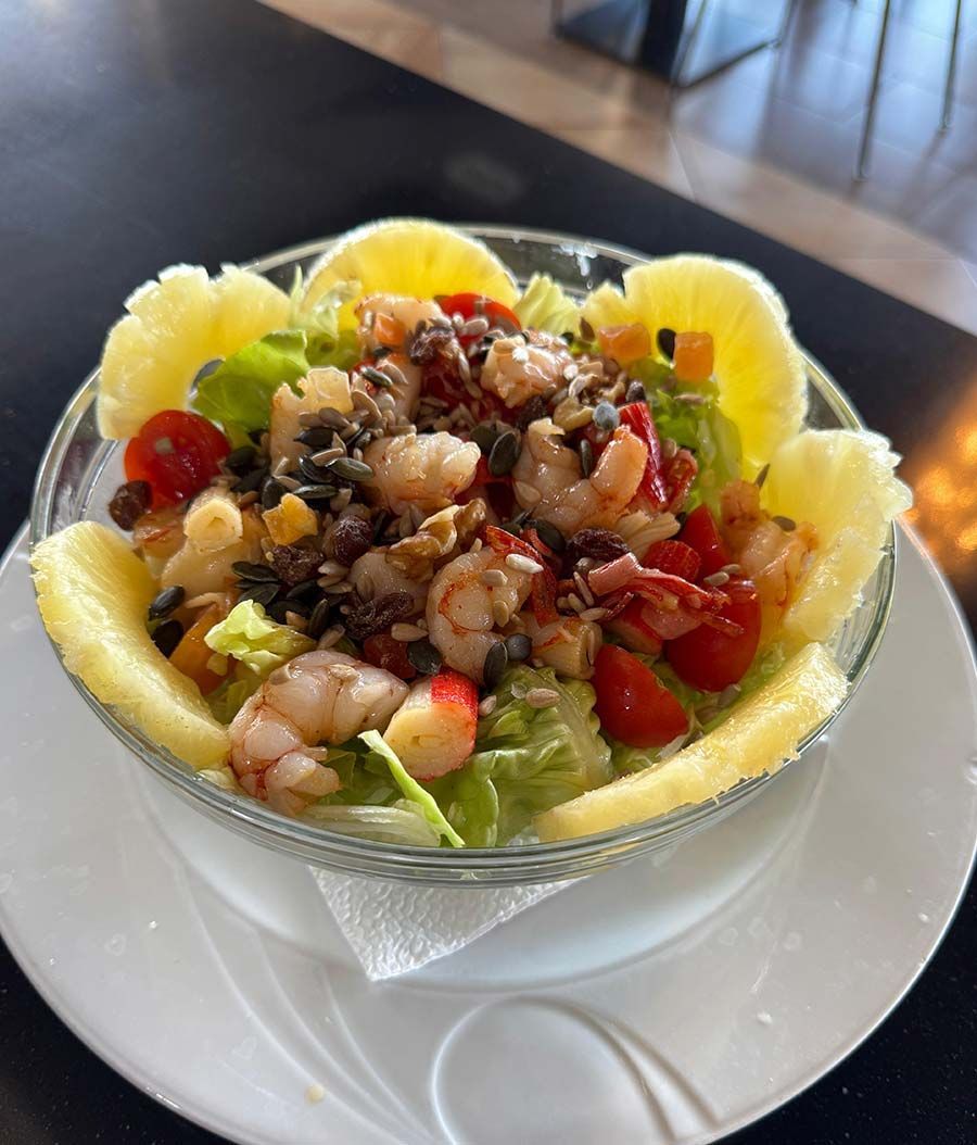 Una ensalada con camarones, piña y tomates en un bol en un plato con una cuchara.