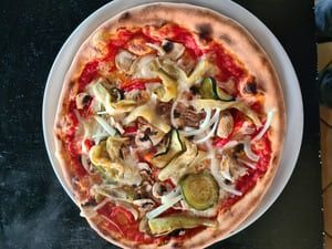 Una pizza con muchas verduras encima está en un plato blanco.