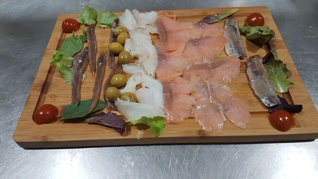 Una tabla de cortar de madera cubierta con carne y verduras sobre una mesa.