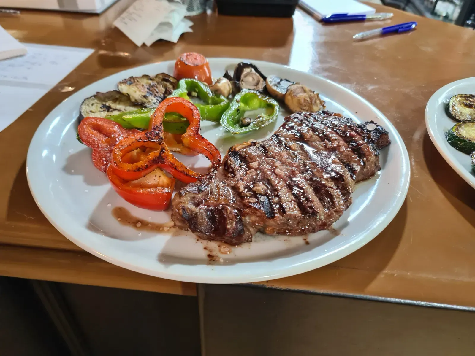 Un plato blanco con un filete y verduras sobre una mesa.