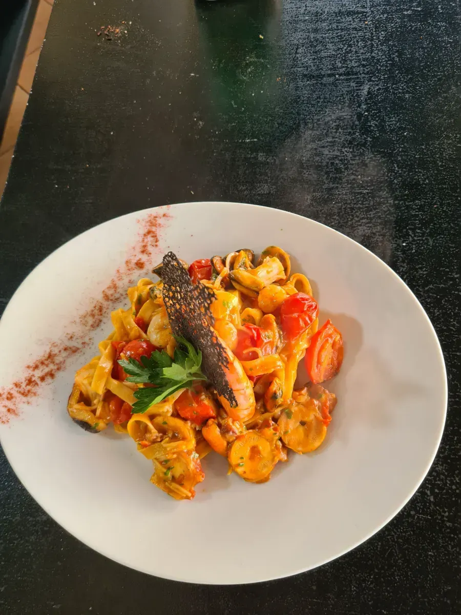 Un plato blanco cubierto con pasta, tomates y perejil.
