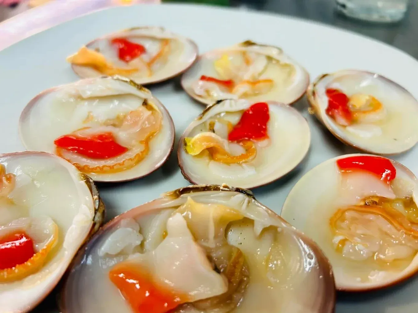 Almejas abiertas en un plato; carne roja y naranja, conchas blancas.