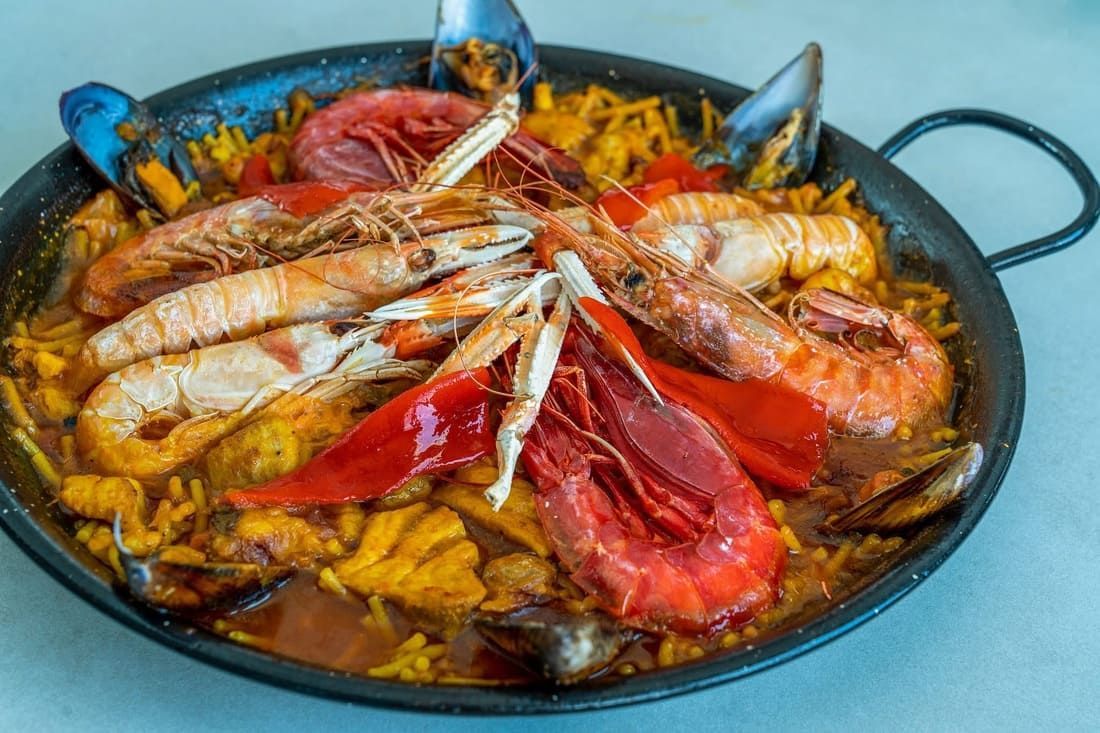 Paella de marisco en una sartén negra con gambas, cangrejo y verduras coloridas.